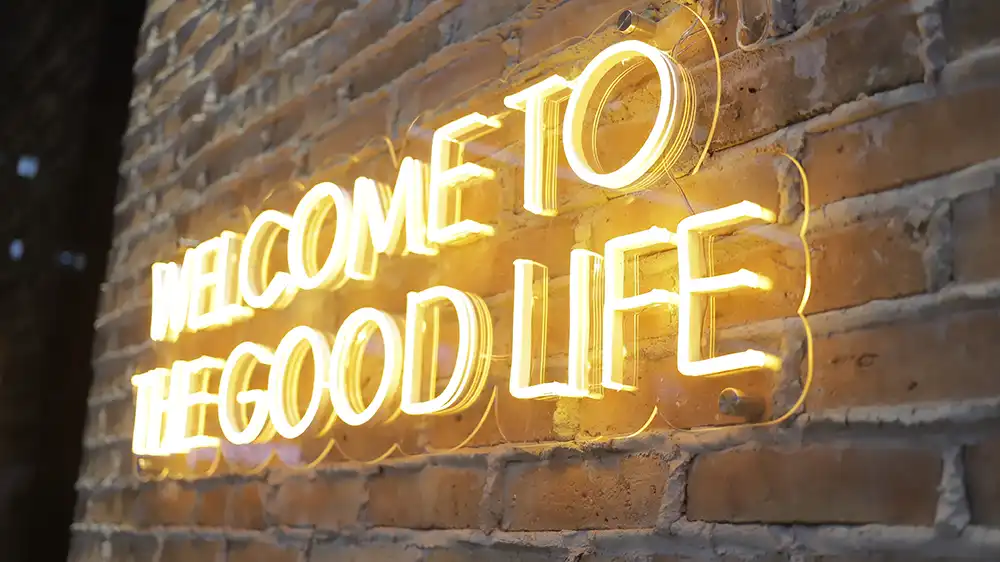 cartel-de-neon-naranja-que-dice-bienvenido-la-buena-vida-en-el-fondo-de-la-pared-de-ladrillo_copy.webp